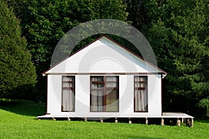 Small white house with curtained windows stands on a small slope, front view