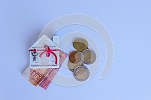 A small white house is decorated with a decorative key on a red ribbon. Euro bills and coins.