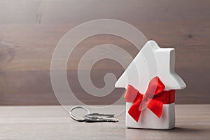 Small white house decorated red bow ribbon with bunch of keys on wooden background. Gift, real estate or buying a new home