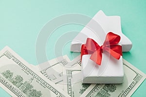 Small white house decorated red bow ribbon and dollars money on green background. Buying a new home, gift or sale of real estate.