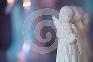 Small white marble figurine of an angel on a pearlescent pink blue blurred bokeh background.