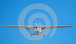 Small white plane with blue stripes of a cessna propeller flying in a clear sky before landing on Sabadell Airport