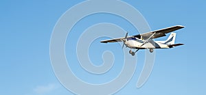 Small white plane with blue stripes of a cessna propeller flying in the evening light in a clear blue sky before landing at