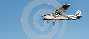 Small white plane with blue stripes of a cessna propeller flying from side view point of view in a clear blue cloudless sky before