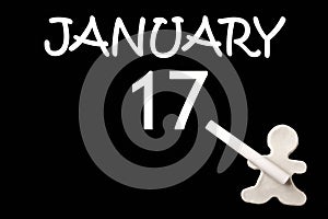 A small white plasticine man writing the date 17 January on a black board. Business concept. Education concept.