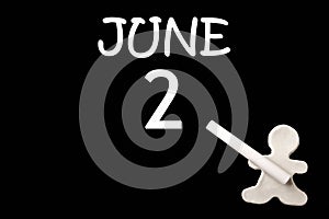 A small white plasticine man writing the date 2 June on a black board. Business concept. Education concept.