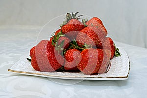 Small white plate, filled with succulent juicy fresh ripe red strawberries