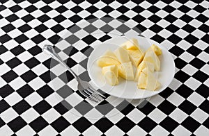 Plate of pineapple slices with a fork on a tablecloth