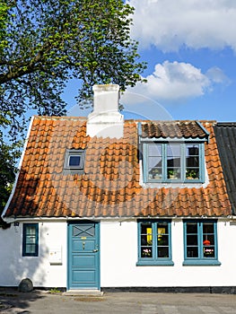 A small white romantic house with a clay tile roof and a white chimney against a blue sky background