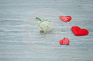 Small white rose with soft, silk red hearts on the background of a wooden table. Declaration of love.