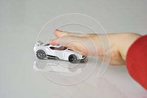 Small white toy car, pushed by children`s hand. The hand is defo