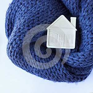 Small white toy house lies on a warm cozy scarf. Concept-insula