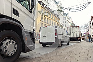 Small white van and mid size cargo truck parked for unloading at european old city street road. Fast express courier