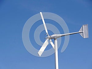 Small white wind turbine, windmill alternative Green clean energy against blue sky