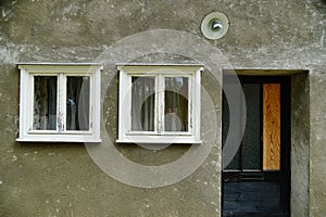 Small white window and a door with a gray concrete wall of an abandoned house in Germany