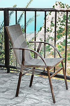 A small wicker chair or cane-chair on terrace or balcony with a beautiful view of the top of the rock, the blue sea and sky