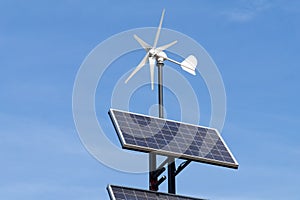 Small wind power generator and set of Solar panels agains blue sky.