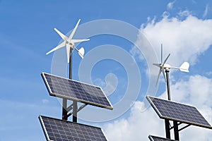 Small wind power generators and set of Solar panels agains blue sky with white clouds.