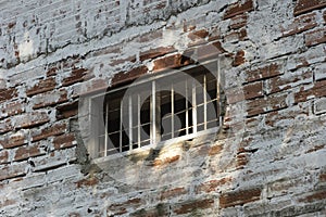 Small window with bars on old wall of old brick house with white and copper colored paint. I lock up in daylight for the virus