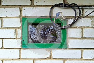 Small window in green wooden frame. Old black wire. Close-up view of cement bonded brick wall.