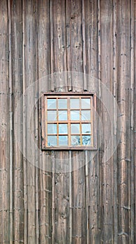 A small window with muntins against the background of a wall covered with wooden boards in a vertical arrangement