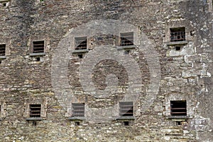 Small windows with metal bars in a jail. Hard conditions. History of criminal correction system. Weathered stone wall. Cork gaol,