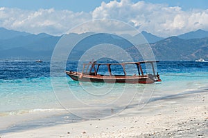 Small wooden boat on blue beach with cloudy sky and Lombok island on background. Gili Trawangan, Indonesia