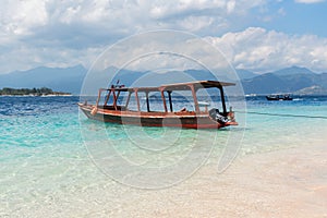 Small wooden boat on blue beach with cloudy sky and Lombok island on background. Gili Trawangan, Indonesia