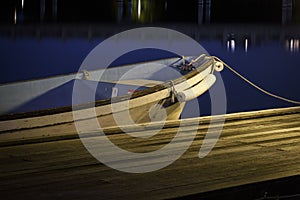 A small wooden boat parked at the dock or pier at night. Night photography with blue smooth waters.