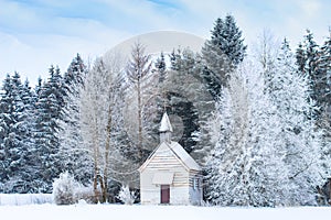 Small wooden chapel on snowbound frosty glade in snowy frozen forest