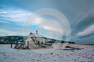 A small wooden Christian church stands among the snows and mountains.