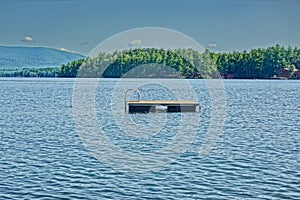 Small wooden dock floats on the calm waters of New Hampshire's Lake Winnipesaukee