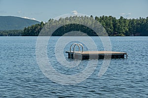 Small wooden dock floats on the calm waters of New Hampshire's Lake Winnipesaukee