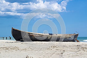 Small wooden fisher`s boat with fishing nets drying on white beach near sealine