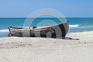 Small wooden fisher`s boat with fishing nets drying on white sandy beach near sealine