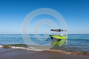 Small wooden green boat anchored on the beach with waves crushing against the shore, Fujairah, United Arab Emirates