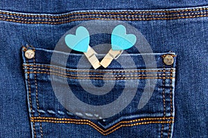 Small wooden heart clothespins fastened to a denim pocket. Small clothespins with blue hearts on the pocket of blue jeans