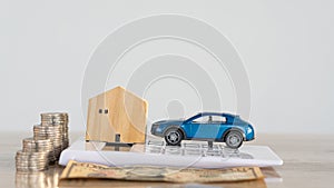 Small wooden house and car on a calculator with piles of coins on the table, car home payment concept.