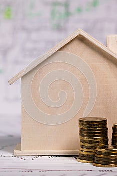 Small wooden house, coins, pen and calculator on technical drawing