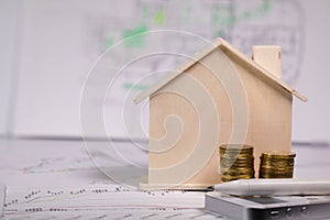 Small wooden house, coins, pen and calculator on technical drawing