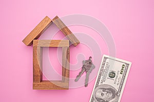 Small wooden house with house keys and US dollars banknote isolated on pink background.