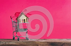 Small wooden house with red bow in supermarket trolley