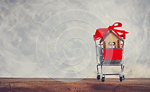 Small wooden house with red bow in supermarket trolley