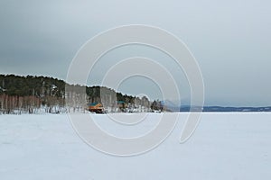 Small wooden houses on the background of blue mountains. Houses on the shore of a frozen lake.