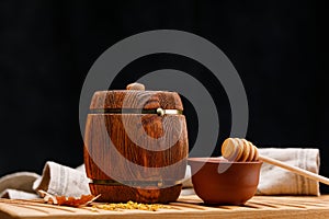A small wooden keg with honey inside and a spoon on a wooden table on a dark background. Barrel. Rustic still life