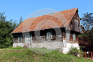 Small wooden old family house with dilapidated boards and broken roof with missing roof tiles on top of small hill