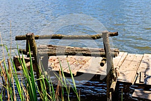 Small wooden pier with bench for fishing on lake