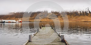 Small wooden pier centered on a lake, facing a snowy mountain photo