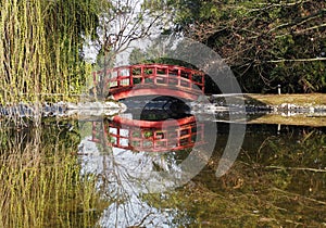 Small wooden red bridge in a woodland with its reflection on a placid river below