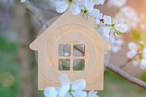 a small wooden toy house in the background of nature, white flowers of an apple tree and sunlight.Close-up, horizontal